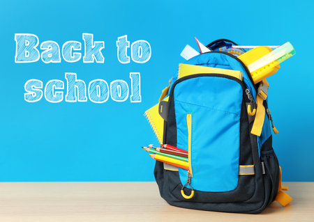 Wooden table with backpack and stationery near text back to school on blue background