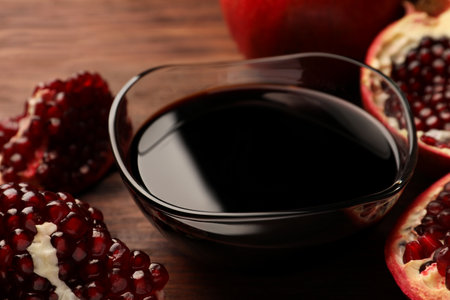 Glass bowl of tasty pomegranate sauce and fresh ripe fruit on wooden table closeup Stock Photo