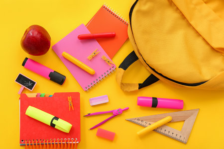 Backpack with fresh red apple and different stationery on yellow background Stock Photo