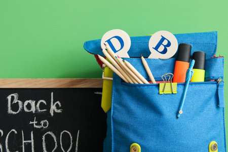 School backpack different stationery and blackboard with text back to school on green background Stock Photo