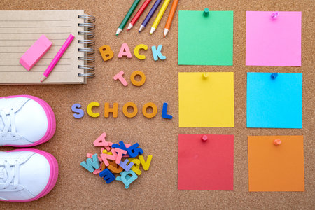 Top view of baby shoes pencils open notepad and blank sheets for notes the inscription back to school place for text or advertisement