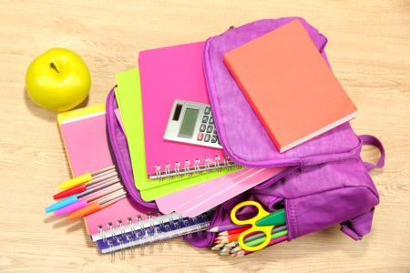 Purple backpack with school supplies on wooden