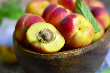 Ripe red apricots in a wooden bowl with mint leaf