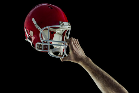 American football player holding up his helmet against black background Stock Photo