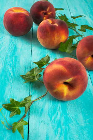 Five ripe peaches on turquoise table with a sprig of ivy selective focus Stock Photo