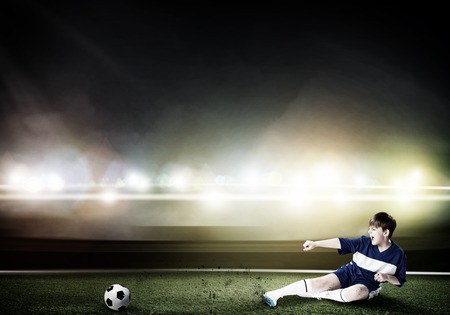 Kid boy kicking soccer ball at stadium field Stock Photo