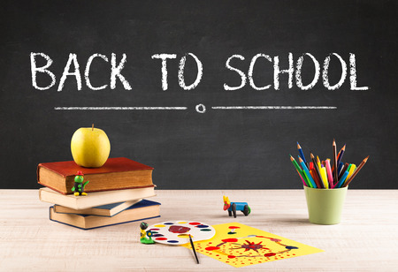 Back to school concept with writing on blackboard in capital letters and a desk with papers fruit