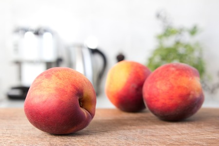 Few colorful juicy peaches on wooden board white modern kitchen at the background