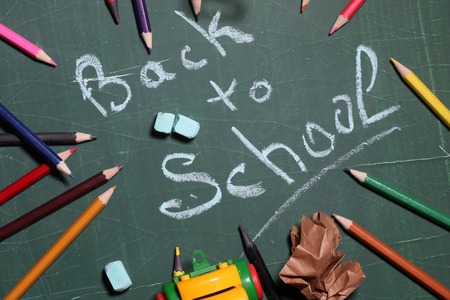 Back to school word text drawing by blue pieces of chalk in center on green blackboard and colored pencils screwed paper and car toy laying around Stock Photo