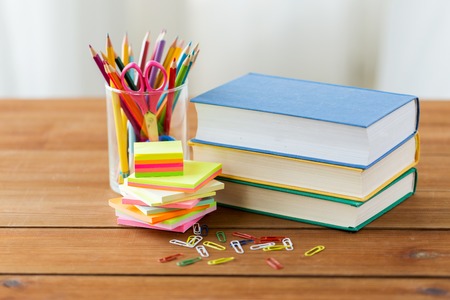 Education school supplies and object concept close up of stand or glass with writing tools and book with scissors on wooden table