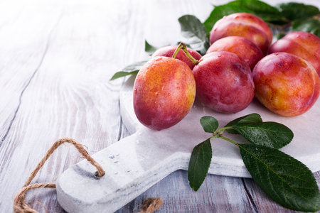 Fresh plums on marble cutting board on old white wooden background selective focus healthy food concept copy space Stock Photo