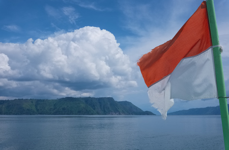 Flag of indonesia flying with cloudy landscape at the background lake toba north sumatra