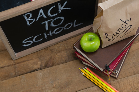 Lunch paper bag green apple and slate with text back to school on wooden table against black background Stock Photo