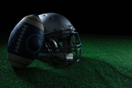 American football leaning on headgear against black background