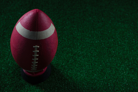 Close up of american football standing on holder on artificial turf against black background