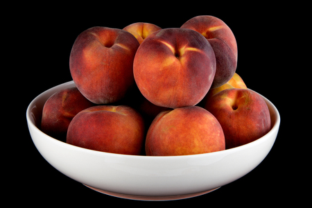 Peaches in a white bowl isolated on a black background