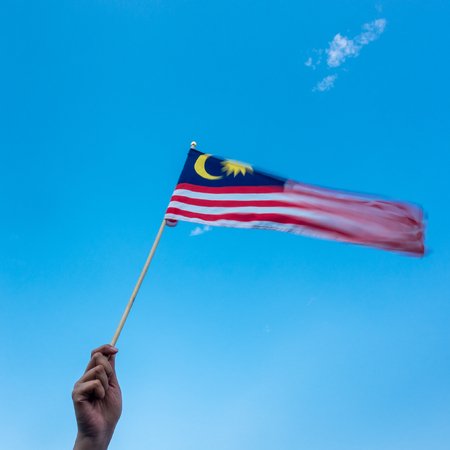 Hand holding malaysia flag wind blowing motion blur on flag blue sky