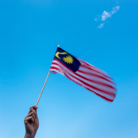 Hand holding malaysia flag wind blowing motion blur on flag blue sky