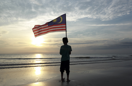 The concept of independence day a boy holding the malaysian flag on the shore at sunrise