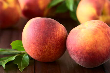 Fresh ripe peaches photographed on dark wood with natural light selective focus focus on the front of the front left peach