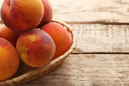 Ripe peaches fruit in basket on wooden table