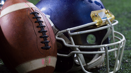 Closeup shot of american football helmets and trophy on grass field at night