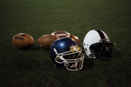 American football and helmets on grass field at night