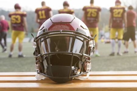 Football helmet on the bench and players behind Stock Photo