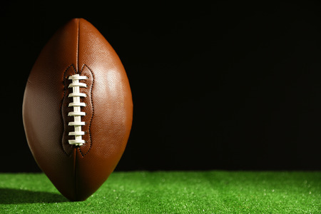 American football on green grass on black background